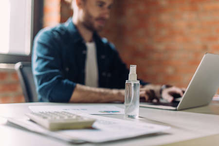 selective focus of bottle with hand sanitizer near businesswoman using laptop in office