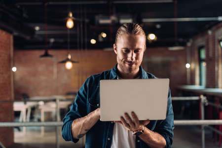 bearded businessman holding and using laptop in modern office