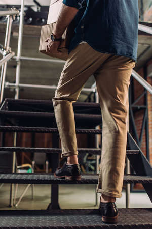 cropped view of businessman holding boxes while walking on stairs in office
