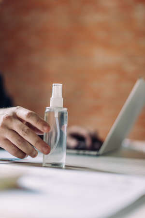 cropped view of businessman touching bottle with hand sanitizer and using laptopの写真素材