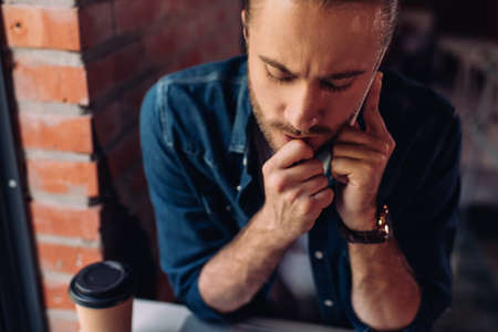 selective focus of pensive businessman talking on smartphone near paper cup with coffee to go