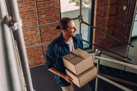 selective focus of smiling businessman holding boxes and walking on stairs in new officeの写真素材