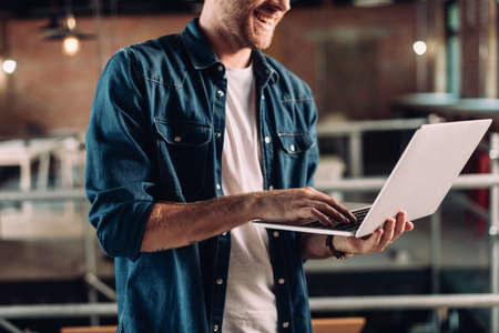 cropped view of happy businessman holding and using laptop in modern office