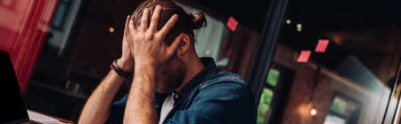 panoramic crop of stressed businessman touching head in officeの写真素材