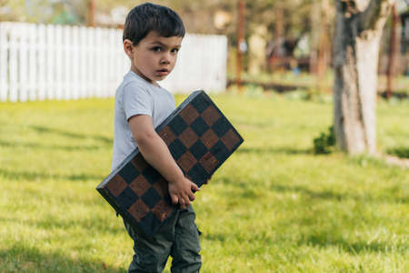 cute kid holding chessboard and looking at cameraの写真素材