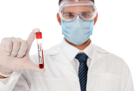 Selective focus of doctor in protective mask and goggles holding test tube with blood sample and...