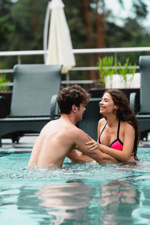 happy muscular man touching cheerful girl in swimming pool