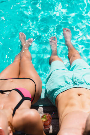 cropped view of couple in swimwear sitting near swimming pool