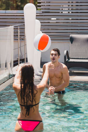 back view of girl and shirtless man playing volleyball with beach ball in swimming pool