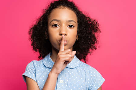 cute curly african american kid showing shh sign isolated on pinkの写真素材