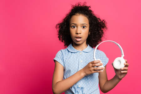 shocked cute curly african american kid with headphones isolated on pinkの写真素材