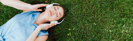 panoramic crop of beautiful woman lying on grass and listening music