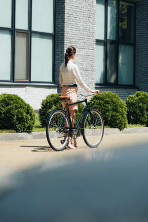 selective focus of businesswoman walking with bicycle near modern buildingの写真素材