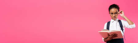 african american schoolgirl in glasses reading book isolated on pink, panoramic shotの写真素材