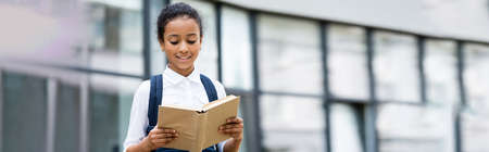 smiling african american schoolgirl reading book outdoors, panoramic shotの写真素材