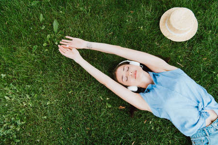 top view of attractive woman lying on grass and listening music near straw hatの写真素材