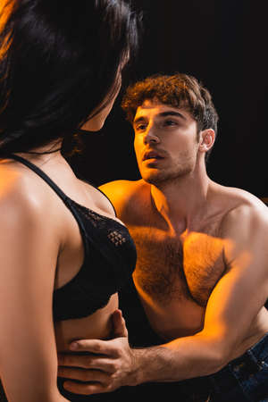 muscular man touching and looking at sexy woman in lace bra isolated on blackの写真素材