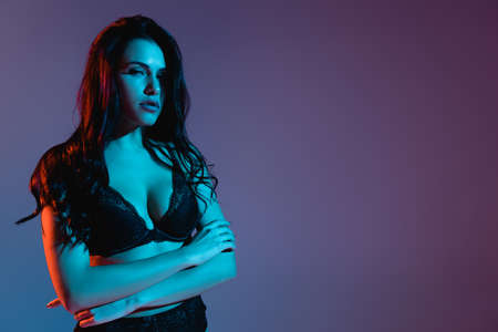 sexy young woman looking at camera while standing with crossed arms isolated on purpleの写真素材