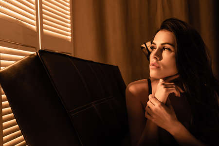 sexy woman lying on black sofa and looking at window blindの写真素材