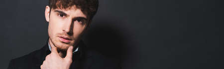 panoramic crop of handsome man touching face and looking at camera on blackの写真素材