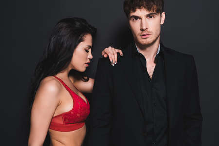sexy woman in red and lace bra touching handsome man on blackの写真素材