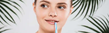 panoramic shot of happy woman smiling near straw and palm leaves on whiteの写真素材