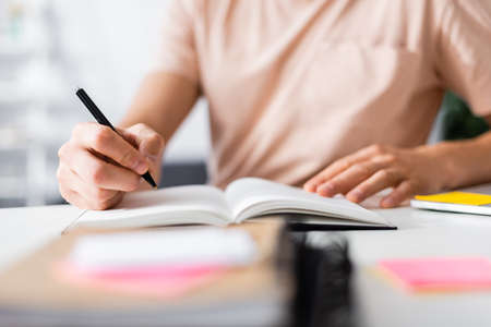 Cropped view of man holding pen near notebook on table at home