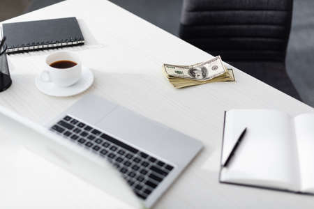 Selective focus of dollars near laptop, notebooks and cup of coffee on table, earning online concept