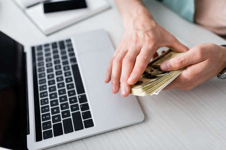 Cropped view of man holding cash near laptop on table, earning online conceptの写真素材