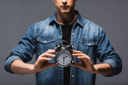 Cropped view of man holding alarm clock isolated on gray, concept of time managementの写真素材