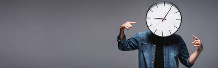 Panoramic crop of man with clock on head pointing with fingers on gray background with copy space,...