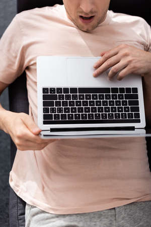 Top view of shocked freelancer using laptop on couch, earning online concept