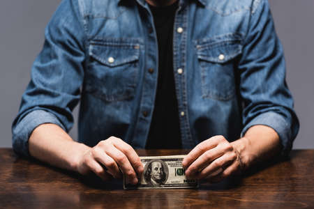 Cropped view of young man holding dollars at table isolated on grayの写真素材
