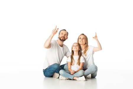 happy family sitting on floor with crossed legs and pointing up isolated on white