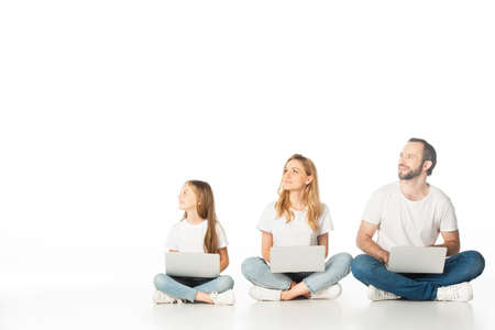 family sitting on floor with laptops on crossed legs and looking away isolated on white