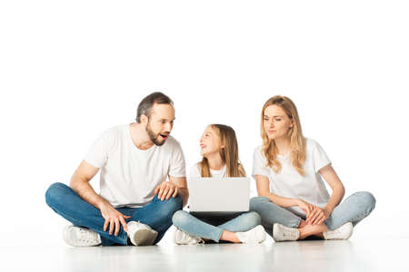parents sitting on floor near happy daughter with laptop isolated on whiteの写真素材