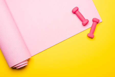 top view of pink fitness mat and dumbbells on yellow background