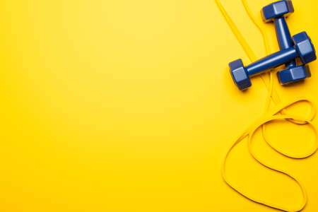 top view of blue dumbbells and resistance band on yellow backgroundの写真素材