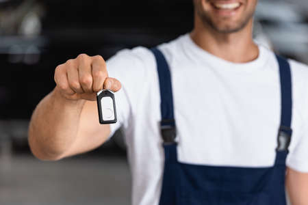 cropped view of happy mechanic in uniform holding car key