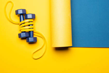 top view of blue fitness mat with dumbbells and resistance band on yellow background