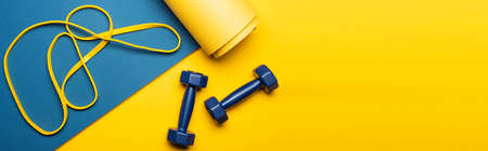 top view of blue fitness mat with dumbbells and resistance band on yellow background, panoramic shotの写真素材