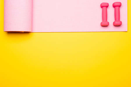 flat lay with pink fitness mat and dumbbells on yellow background