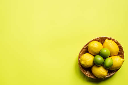 top view of ripe limes and lemons in wicker basket on colorful backgroundの写真素材