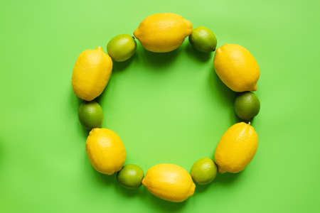 top view of ripe lemons and limes arranged in round empty frame on green backgroundの写真素材