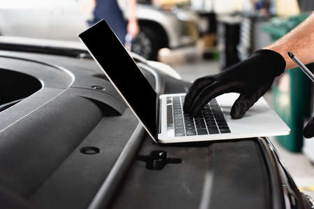 Cropped view of auto mechanic typing on laptop with blank screen on car at service station