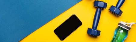 top view of blue fitness mat with dumbbells, smartphone and sports bottle on yellow background, panoramic shotの写真素材