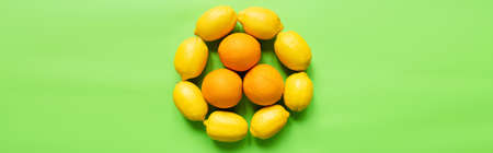 top view of ripe lemons and oranges arranged in circle on green background, panoramic orientation