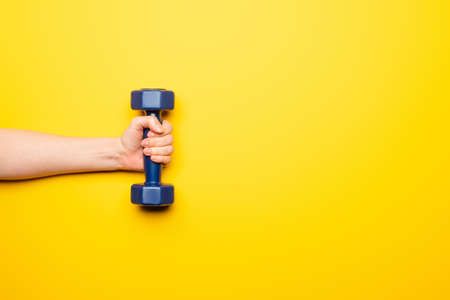 cropped view of woman holding blue dumbbell on yellow background