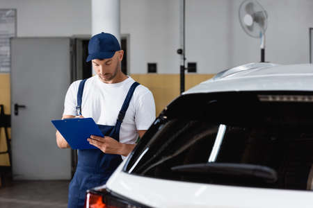 mechanic in cap holding clipboard and writing near carの写真素材