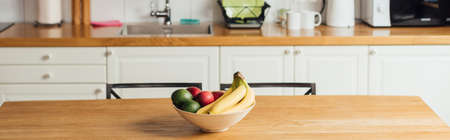 Panoramic shot of fresh fruits in bowl on wooden table in kitchen